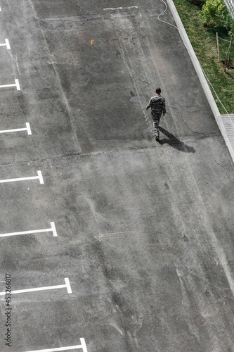 Parking on the street next to the house. A man walks through a new paved empty parking lot with new painted lanes