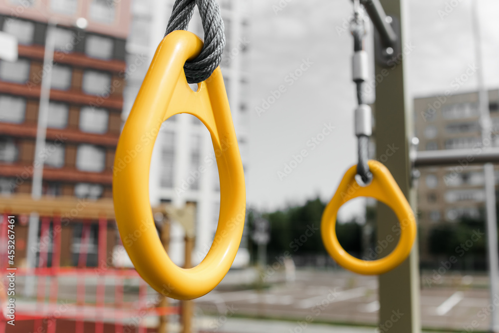 An element of a sports ground. plastic rings for pull-ups. A summer day. Outdoor colorful playground with rubber flooring next to the house. An element of a sports ground. plastic rings for pull-ups. A summer day. Outdoor colorful playground with rubber flooring next to the house.