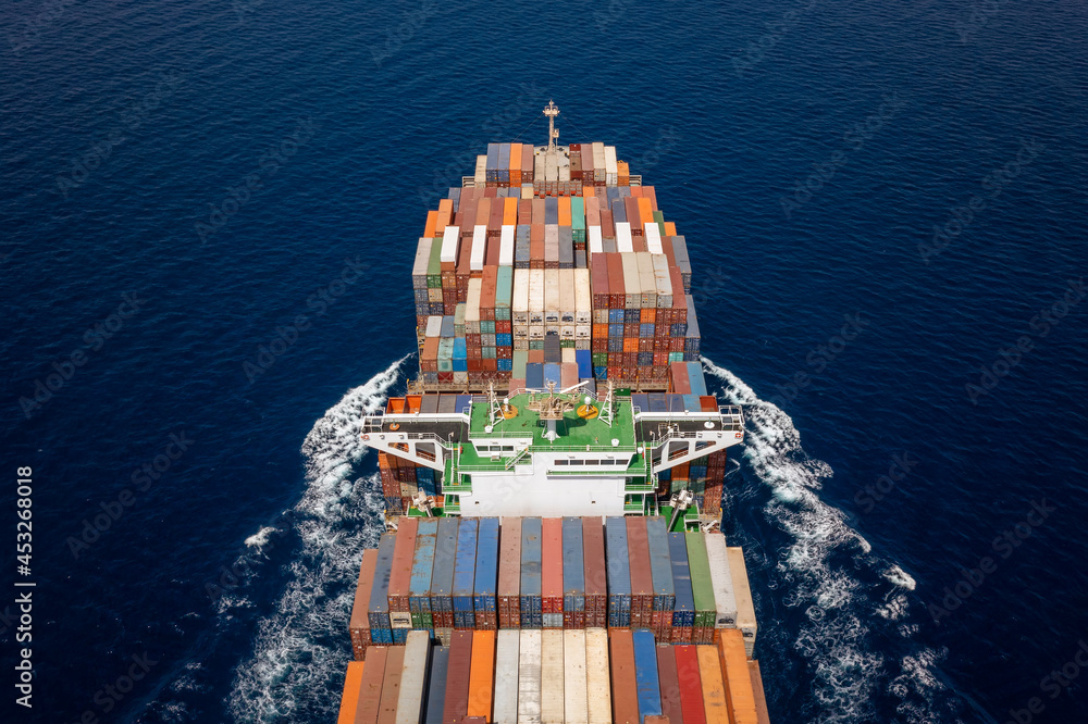 Fototapeta premium Aerial view of a heavy loaded container carrier ship in motion over blue sea
