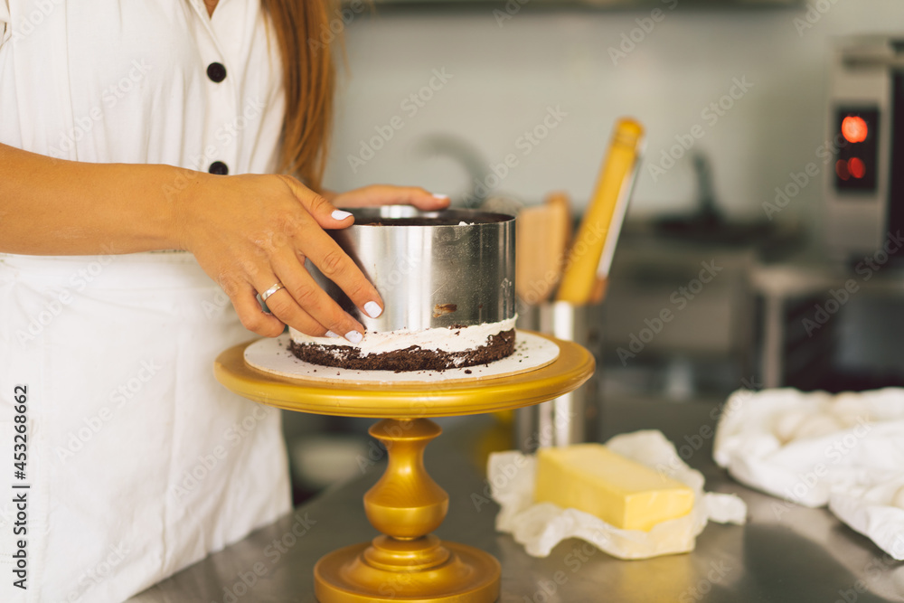 Confectioner girl is preparing a cake biscuit with white cream and chocolate. Cooking cakes.
