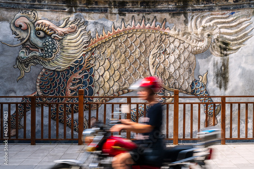 Fototapeta Naklejka Na Ścianę i Meble -  A motorcycle running fast in front of an ancient wall in Guangdong, China. On the wall there's a kylin sculpture.