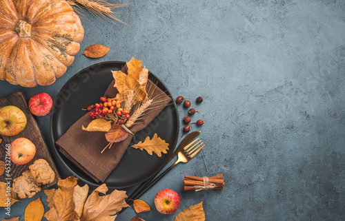 Festive autumn background with cutlery, leaves and pumpkin on a dark background. Top view, copy space.