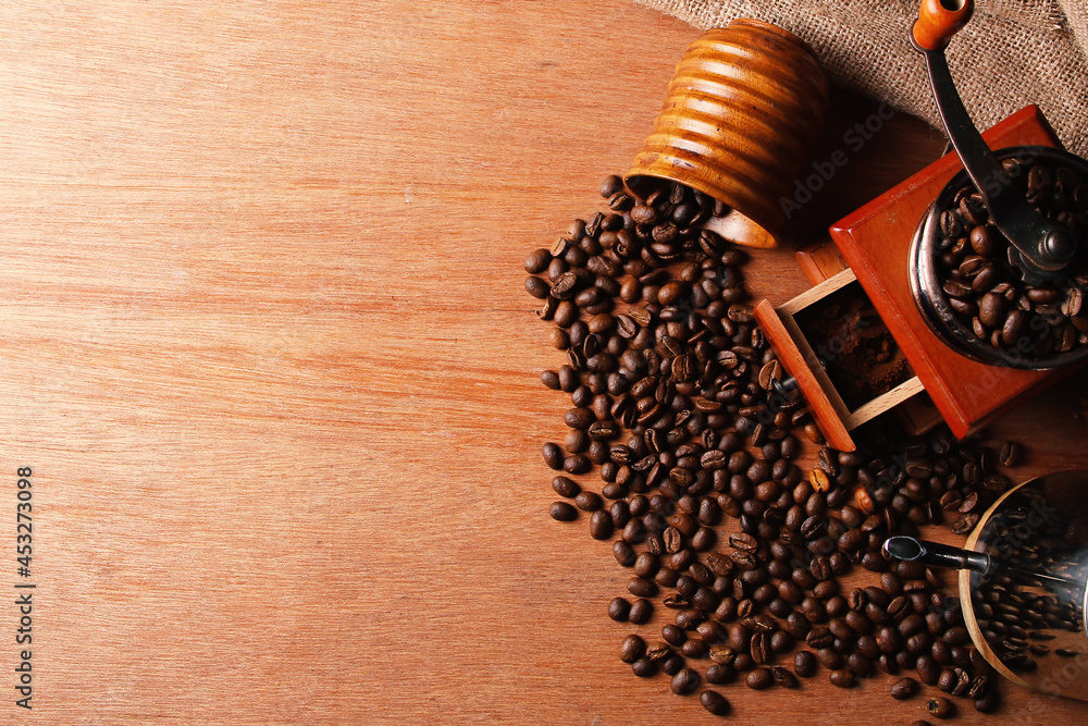 Manual coffee grinder, teapot, and wooden cup with spilled coffee beans