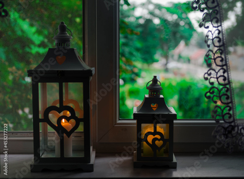 Stojące na parapecie okiennym w mieszkaniu lampiony z płonącymi wewnątrz nich świecami.