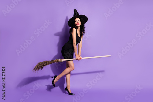 Full size photo of happy smiling good mood beautiful girl witch riding broomstick isolated on purple color background