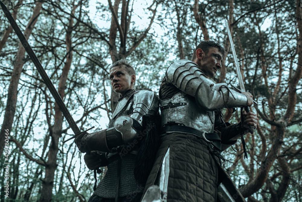 Two medieval knights stand back to back and defend with raised swords. Two medieval knights stand back to back and defend with raised swords.
