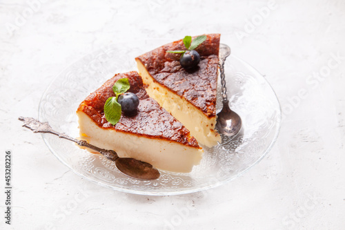 Slice of Homemade Basque burnt cheesecake on a plate with blueberries and mint leaves on light background.