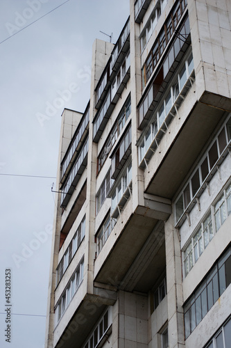 old multi-storey residential building with balconies, located in a poor area, decorated with white tiles against a gray cloudy sky
