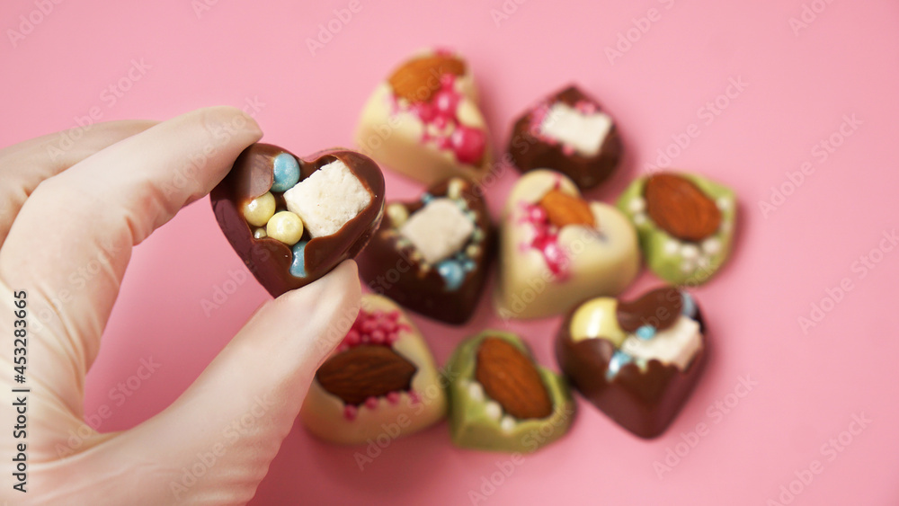 Pastry chef's hand in gloves holds a heart-shaped candy. Sweets on a pink background. Valentine's Day Candy