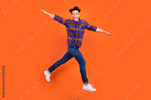 Photo of pretty funny teen boy wear plaid outfit spectacles smiling arms sides isolated orange color background