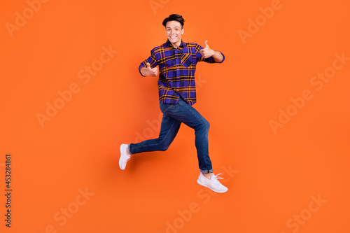 Full size profile photo of young cool guy jump show thumb up wear shirt jeans sneakers isolated on orange background © deagreez