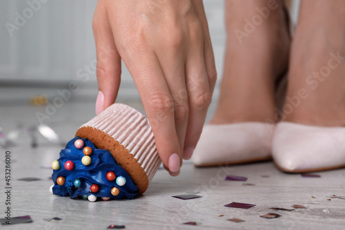 Woman picking up dropped cupcake from floor, closeup. Troubles happen