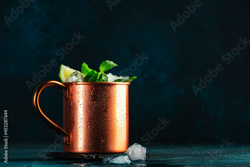 Moscow mule cocktail in copper mug with lime, ice, ginger beer, vodka and mint. Deep blue background photo
