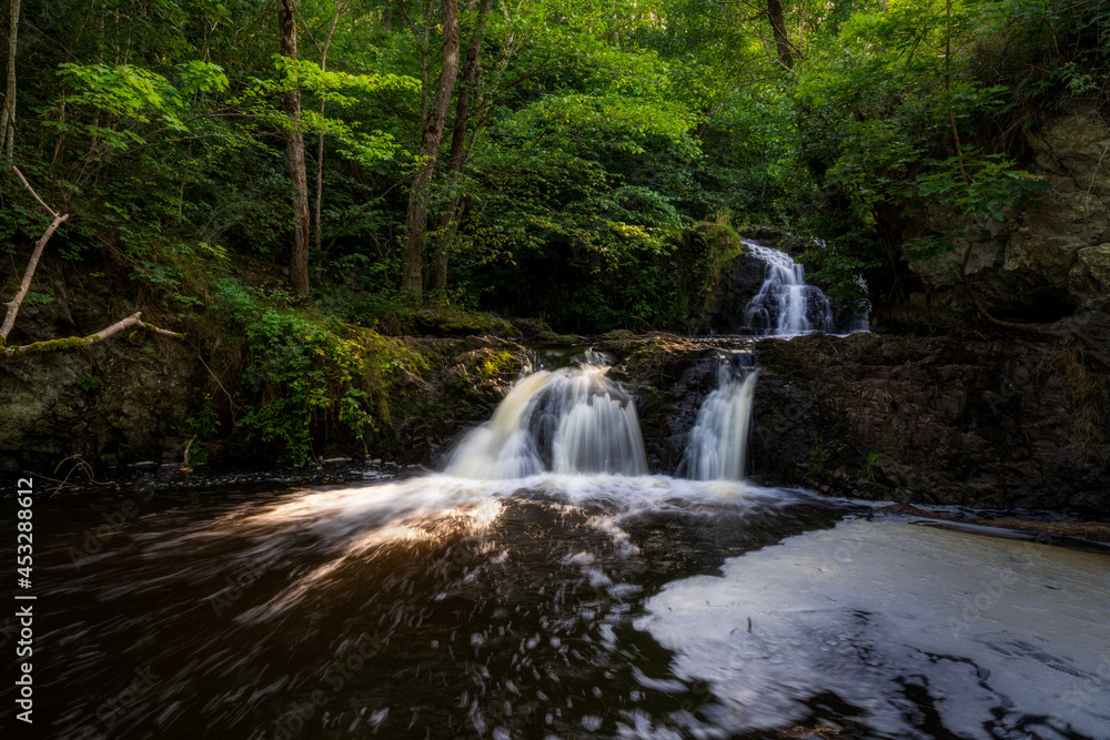 Gorgeous golden hour light through trees is lighting up the beautiful waterfall.