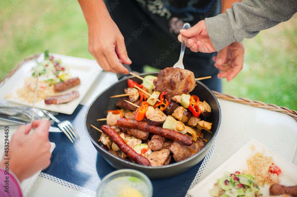 BBQ grilling party. Close up of people hands taking barbecue and grilled vegetables skewers