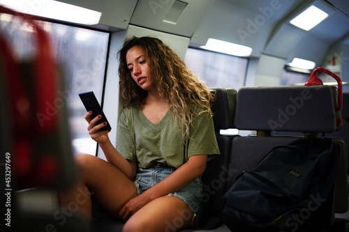 Young beautiful girl tourist travels by train. Happy smiling woman using the phone while travel by train. © JustLife
