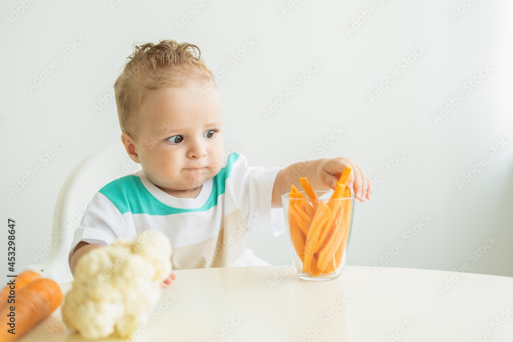 Baby boy sitting in a Childs chair eating carrot slices on white background. Baby boy sitting in a Childs chair eating carrot slices on white background.