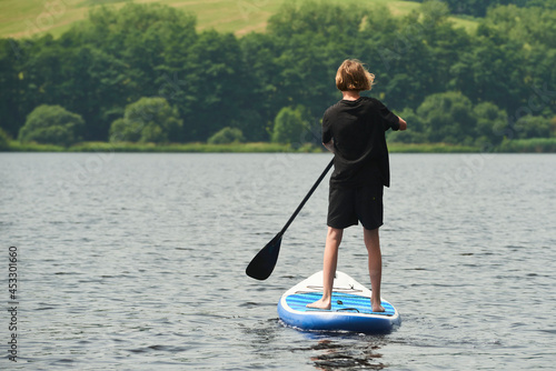 Boy rowing on stand up paddle boarding (SUP) paddling along the calm lake. The concept of children's sports and tourism.  © Petr Bonek