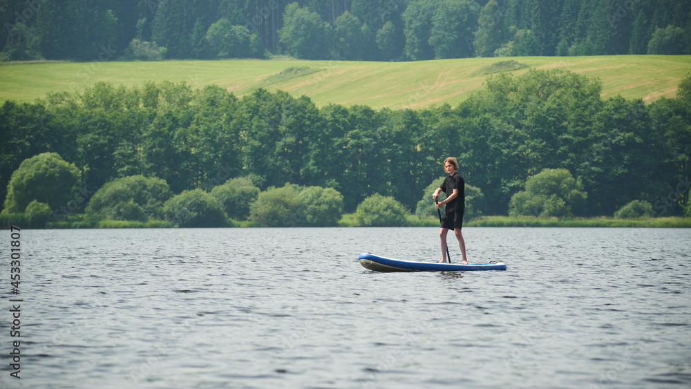 Boy rowing on stand up paddle boarding (SUP) paddling along the calm lake. The concept of children's sports and tourism.
Boy rowing on stand up paddle boarding (SUP) paddling along the calm lake. The concept of children's sports and tourism.