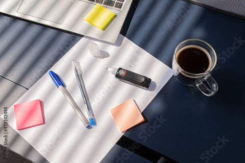 business table chancellery equipment white sheet of paper, pens, concealer, laptop, colorful stickers, eraser and sun cup of coffee
