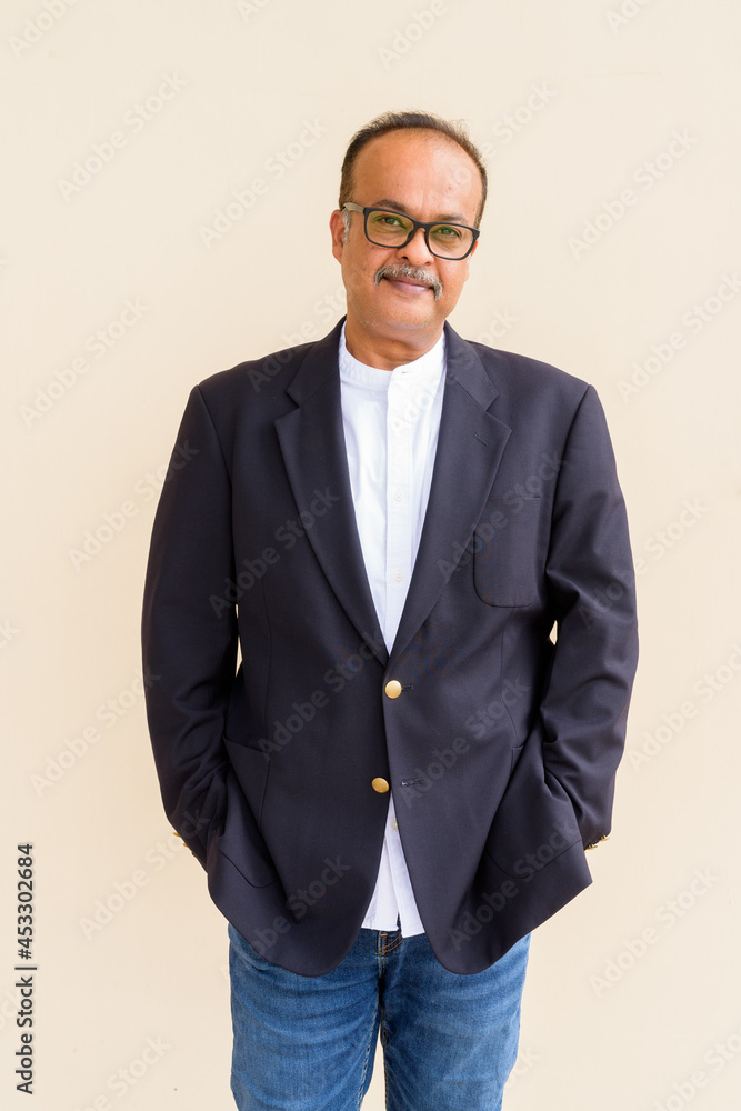 Fototapeta premium Portrait of handsome Indian businessman with mustache wearing hat against plain wall