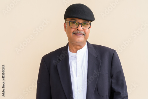 Portrait of handsome Indian businessman with mustache wearing hat against plain wall