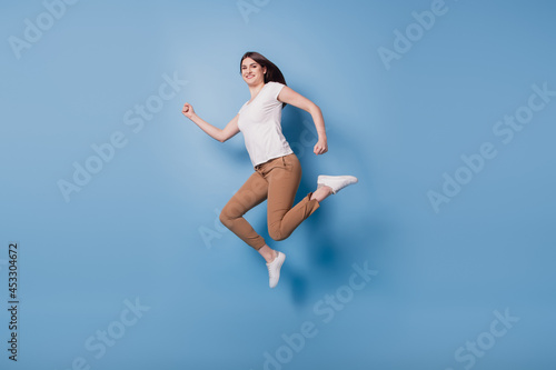 Fototapeta Naklejka Na Ścianę i Meble -  Portrait of sporty energetic active runner lady jump hurry run on blue background