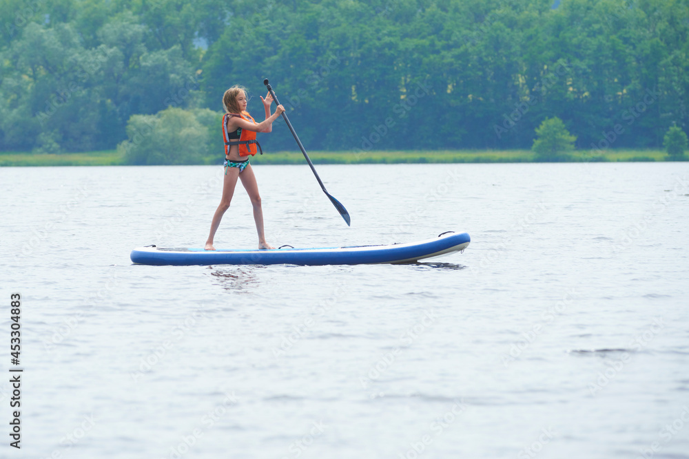 Naklejka premium Paddle boarder. Child girl paddling on stand up paddleboard. Healthy lifestyle. Water sport, SUP surfing tour in adventure camp on active family summer beach vacation. 