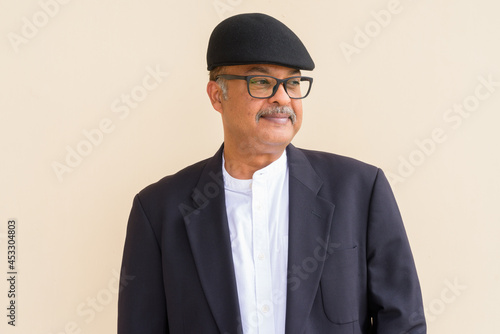 Portrait of handsome Indian businessman with mustache wearing hat against plain wall