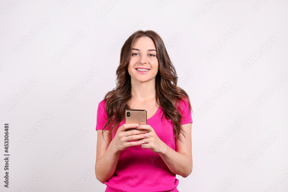 Young beautiful brunette woman with long wavy hair wearing pink shirt, posing with a phone over white isolated background. Portrait of female model showing gestures and emotions. Close up, copy space. Young beautiful brunette woman with long wavy hair wearing pink shirt, posing with a phone over white isolated background. Portrait of female model showing gestures and emotions. Close up, copy space.