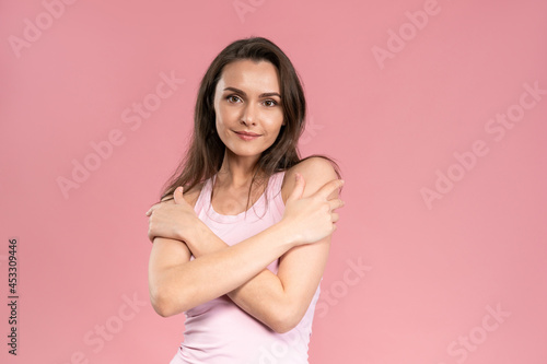 Beautiful young woman with no makeup standing with hands crossed on her chest  attractive brunette girl on pink background. Human emotions  facial expression concept. 