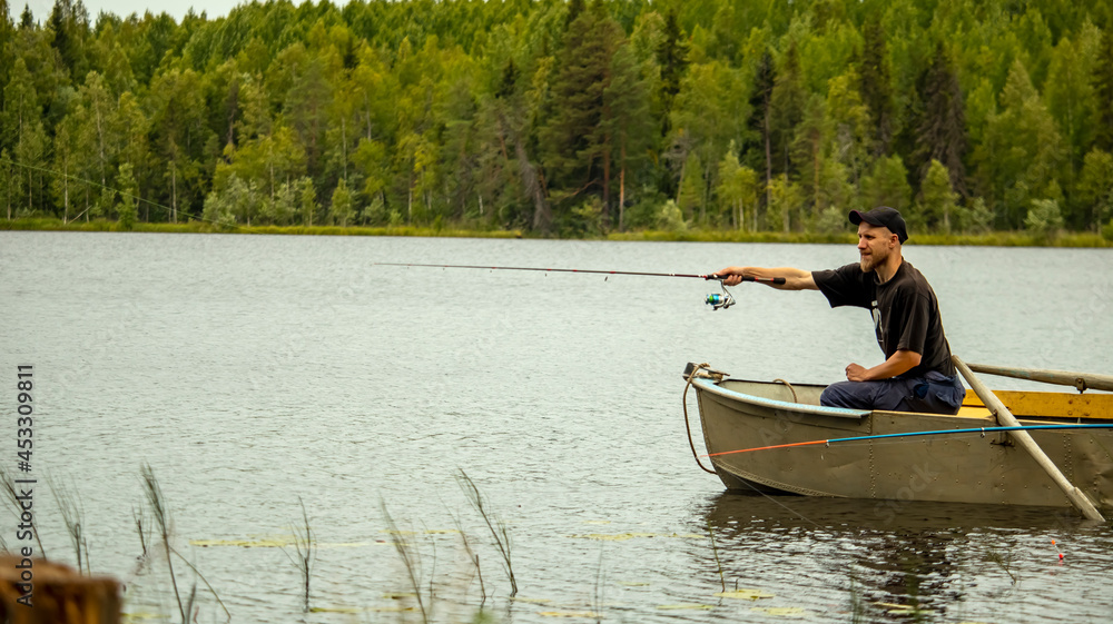 a bearded man is fishing on a spinning rod from a boat on a lake in the forest