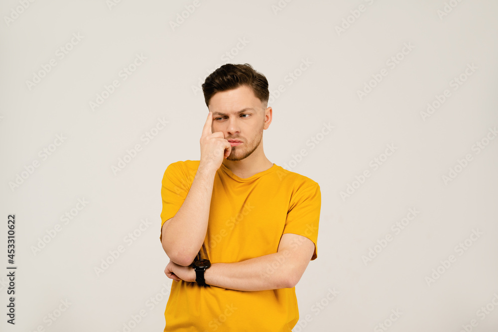 Lost in thought or deep in thought handsome young man folded his hands and holding his face with his hand. Young casual man in yellow t-shirt portrait isolated on white background. Lost in thought or deep in thought handsome young man folded his hands and holding his face with his hand. Young casual man in yellow t-shirt portrait isolated on white background.