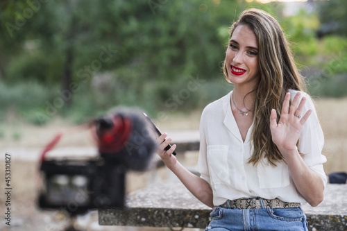 Young Spanish female blogger using her phone and recording herself with a DSLR camera in a park