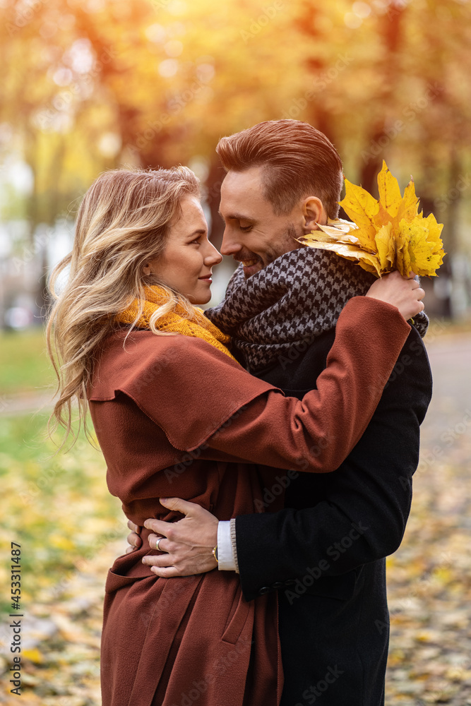 Half-length portrait of a kissing young couple. Husband and a wife hugged smile looking at each other in the autumn park. Outdoor shot of a young couple in love in a autumn park. Half-length portrait of a kissing young couple. Husband and a wife hugged smile looking at each other in the autumn park. Outdoor shot of a young couple in love in a autumn park.