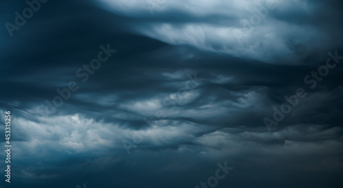 Photograph of a dramatic isolated Asperitas cumulus thunderstorm cloud as it swirls and moves across the sky bringing rain with dark blue textures and undulating ripples and waves of light.