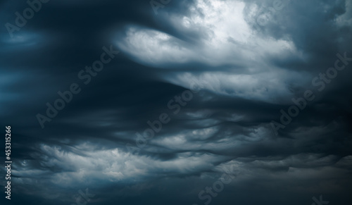 Photograph of a dramatic isolated Asperitas cumulus thunderstorm cloud as it swirls and moves across the sky bringing rain with dark blue textures and undulating ripples and waves of light.