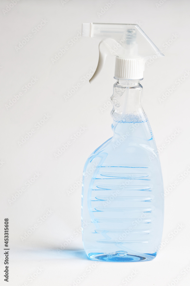 Transparent container with a spray bottle and light blue disinfectant liquid on a white background. Cleanliness, disinfection and cleaning concept Transparent container with a spray bottle and light blue disinfectant liquid on a white background. Cleanliness, disinfection and cleaning concept
