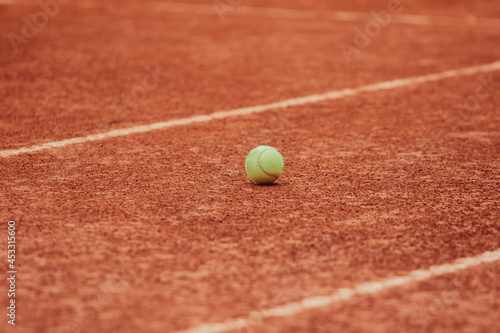 One tennis ball placed on a red clay court between two white lines