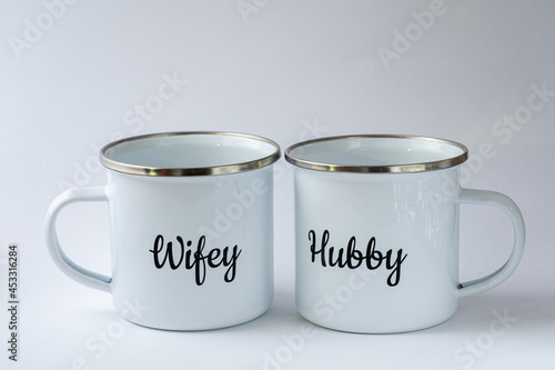 Photography Two white enamel mugs with writings Hubby and Wifeyon them on a white background