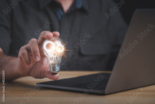 Фотография The hand of a man with a light bulb and he is using a laptop