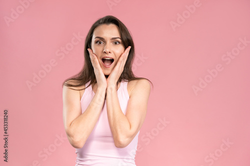 OMG surprised pretty young woman wearing pink t-shirt with hands on her face, excited and joy expression on her face with positive emotions. Facial expressions, emotions, feelings.