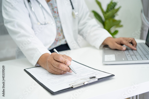 Doctor write health medical note in clipboard with laptop in hospital.