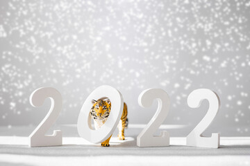Number 2022 and figurine of tiger isolated on grey background with snow. Tiger symbol of the Chinese new year 2022.