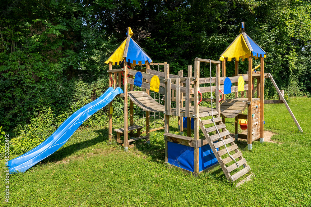 Spielturm für Kinder mit Häusern, Wackelbrücken, Leiter und Rutsche auf einer Wiese im Park