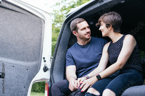 Obraz na płótnie Young couple sitting on a camper van looking at each other and enjoying a good time while travelling. Enjoying simple pleasures. w salonie