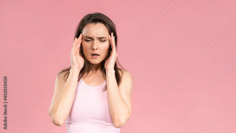 Have a migraine or severe headache while massaging the temporal lobe of the head young woman wearing pink t-shirt holding hands on head. Human emotions, facial expression concept. Have a migraine or severe headache while massaging the temporal lobe of the head young woman wearing pink t-shirt holding hands on head. Human emotions, facial expression concept.