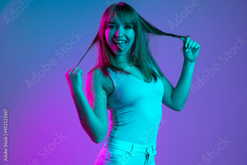 One young beautiful girl having fun isolated on blue studio background in neon light filter. Concept of human emotions, facial expression, youth, sales, ad.