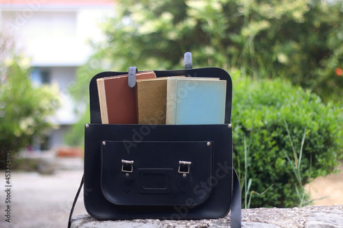 Black satchel bag filled with books. Selective focus. Back to school concept. 