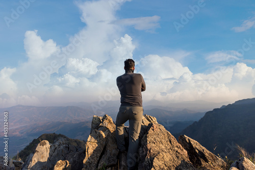 Young Man Standing on the edge of a cliff and enjoys the sunrise. Backpacker in a hike in the summer mountains. A young man on top of the mountain